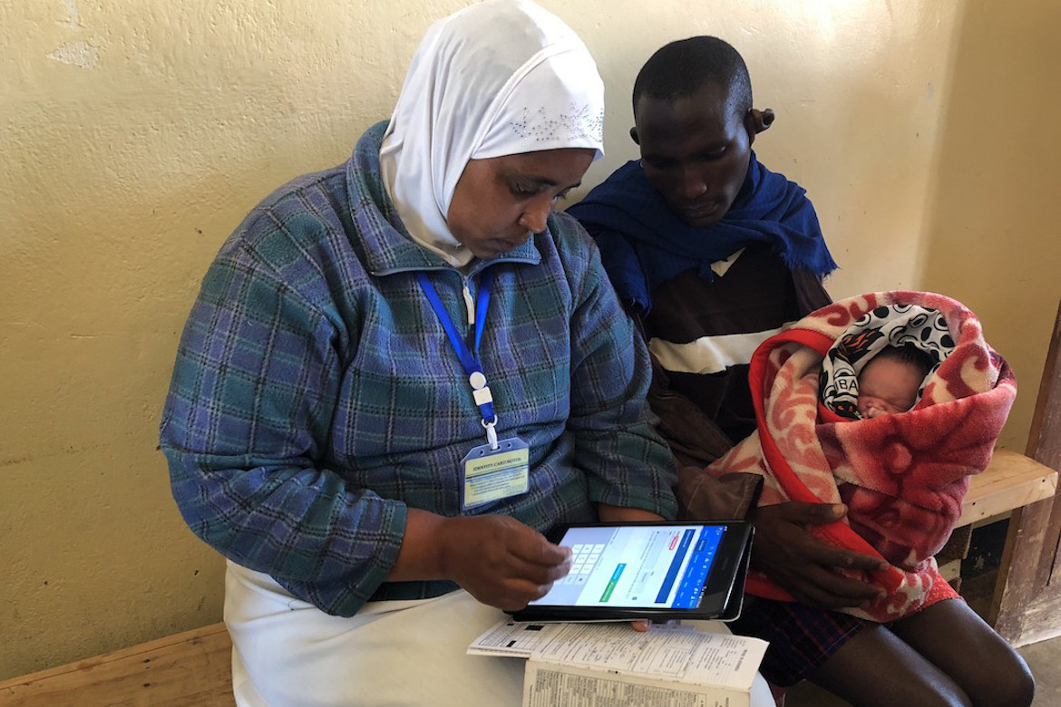A female health worker records immunisation data for a father and his child